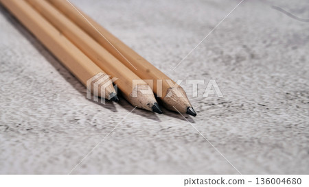Three neatly sharpened light wooden pencils lie together on a speckled grey surface Three neatly sharpened light wooden pencils lie together on a speckled grey surface 136004680