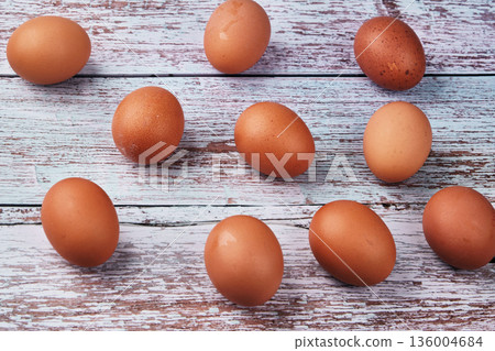 Nine brown eggs rest on a light blue and white distressed wooden surface. These fresh eggs are ideal for cooking or baking delicious meals at home 136004684