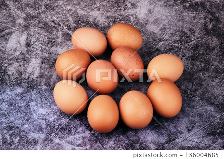 Ten brown chicken eggs are casually arranged on a dark, mottled background. They appear ready for use in a morning breakfast or for baking ingredients in the kitchen 136004685
