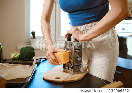 A woman grates cheese over a cutting board A woman grates cheese over a cutting board 136006210