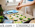 Woman sprinkles pepper over broccoli on a baking tray 136006218