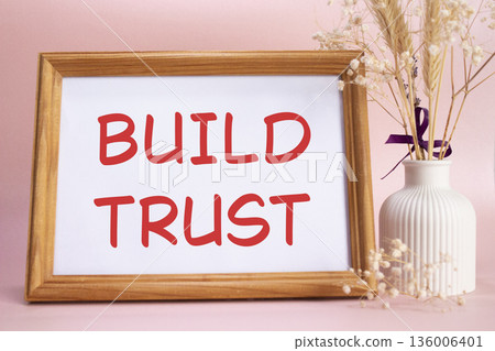 Build trust symbol. Concept words Build trust on beautiful wooden picture frame. Beautiful pink background with flower vase. Business and Build trust concept. Copy space. Build trust symbol. Concept words Build trust on beautiful wooden picture frame. Beautiful pink background with flower vase. Business and Build trust concept. Copy space. 136006401