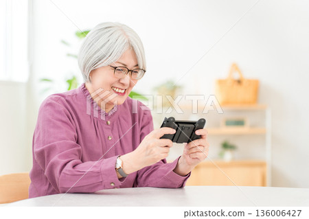 A gray-haired Asian woman playing games in the living room at home 136006427