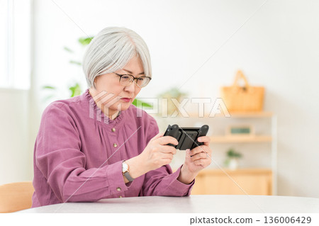 一位頭髮花白的亞洲婦女在家裡的客廳玩遊戲。 136006429