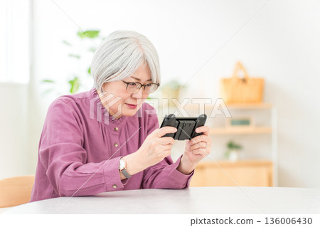 一位頭髮花白的亞洲婦女在家裡的客廳玩遊戲。 136006430