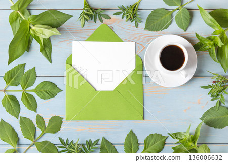 Green envelope with clean white sheet of paper for your text, cup of black coffee and leaves dahlias on blue wooden background. Invitation to the holidays. Flat lay. Green envelope with clean white sheet of paper for your text, cup of black coffee and leaves dahlias on blue wooden background. Invitation to the holidays. Flat lay. 136006632