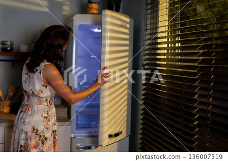 Evening kitchen activity, Lady opens fridge late at night, Woman in floral outfit seeks jar in darkness, Night example of woman retrieving item from cold storage Evening kitchen activity, Lady opens fridge late at night, Woman in floral outfit seeks jar in darkness, Night example of woman retrieving item from cold storage 136007519