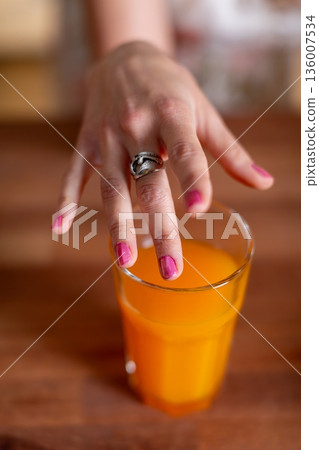 Closeup juice hand, Closeup of hand with pink nails holding juice glass in warm light, Intimate image capturing hand with pink nails and silver ring holding glass of amber juice 136007534