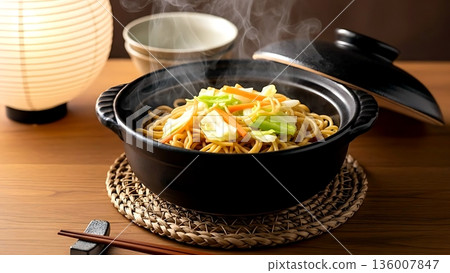Still life, Wabi-sabi aesthetic. a rustic, black-glazed donabe clay pot filled with aromatic yakisoba noodles, strands of cabbage, carrot peeking out  136007847