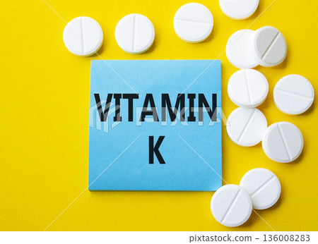 Vitamin K symbol. Concept word Vitamin K on blue note. Beautiful yellow background with pills. Medicine and Vitamin K concept. Copy space 136008283