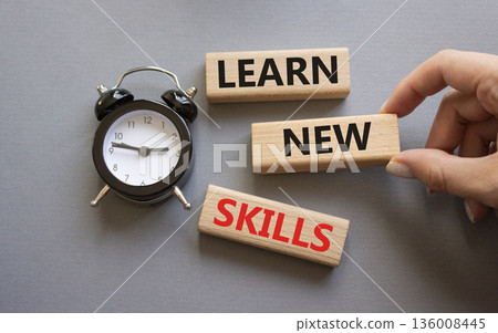 Learn new skills symbol. Concept words Learn new skills on wooden blocks. Businessman hand. Beautiful grey background with alarm clock. Business and Learn new skills concept. Copy space. 136008445