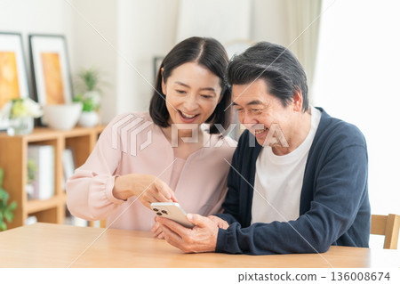 A middle-aged couple watching a smartphone in the living room A middle-aged couple watching a smartphone in the living room 136008674