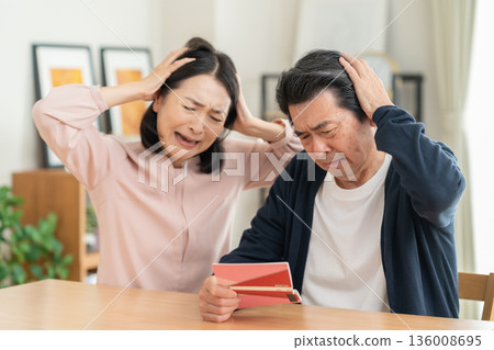 A middle-aged couple looking at their savings passbook in the living room A middle-aged couple looking at their savings passbook in the living room 136008695
