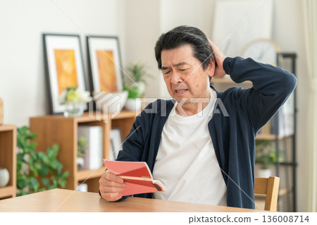 A middle-aged man looking at his savings passbook in the living room 136008714