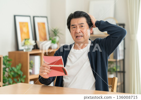 A middle-aged man looking at his savings passbook in the living room 136008715