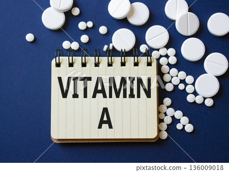 Vitamin A symbol. Concept word Vitamin A on notebook. Beautiful deep blue background with pills. Medicine and Vitamin A concept. Copy space 136009018