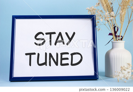 Stay Tuned symbol. Concept words Stay Tuned on beautiful wooden picture frame. Beautiful light blue background with flower vase. Business and Stay Tuned concept. Copy space. Stay Tuned symbol. Concept words Stay Tuned on beautiful wooden picture frame. Beautiful light blue background with flower vase. Business and Stay Tuned concept. Copy space. 136009022