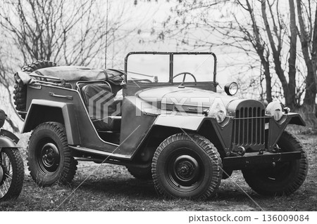 Willys Mb (jeep, U.s. Army Truck, 4x4) Of Us Army Forces Of World War 2 Time Standing Parked At Forest During Reconstruction Of Some Fight World War II. Black And White Colors Willys Mb (jeep, U.s. Army Truck, 4x4) Of Us Army Forces Of World War 2 Time Standing Parked At Forest During Reconstruction Of Some Fight World War II. Black And White Colors 136009084