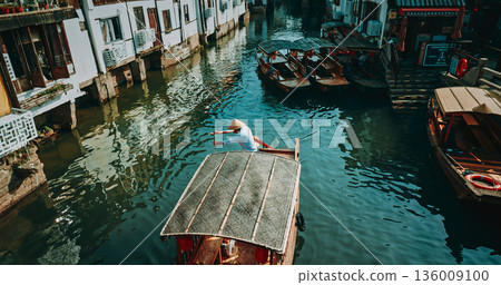 Charming boatman steering through serene waters in a traditional canoe. Zhujiajiao, Shanghai, China 136009100