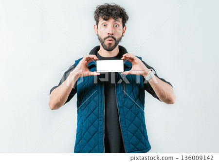 A surprised bearded man showing phone screen isolated. Shocked bearded guy showing promotion on screen phone A surprised bearded man showing phone screen isolated. Shocked bearded guy showing promotion on screen phone 136009142