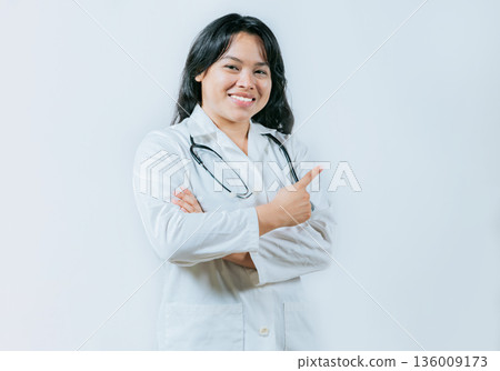 Asian female doctor pointing to the side isolated. Young asian doctor recommending an advertisement 136009173
