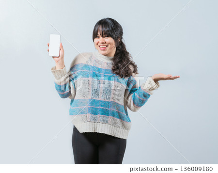 Smiling asian girl showing phone screen isolated. Beautiful asian young woman showing an advertisement on phone screen 136009180