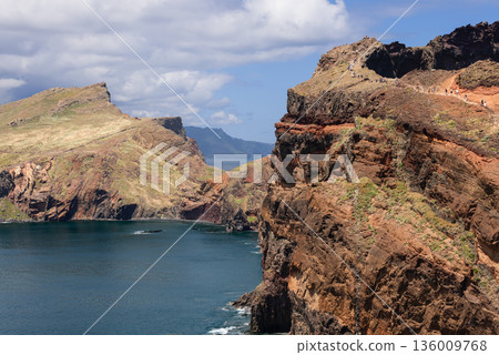 Volcanic cliffs and hiking trail at Baia d Abra with layered rock walls above calm bay Atlantic Volcanic cliffs and hiking trail at Baia d Abra with layered rock walls above calm bay Atlantic 136009768