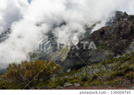 Pico Ruivo ridge in morning fog with jagged volcanic cliffs and slopes emerging above clouds Pico Ruivo ridge in morning fog with jagged volcanic cliffs and slopes emerging above clouds 136009795
