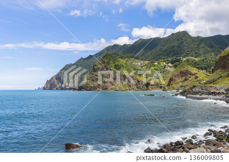 Madeira coastal cliffs and blue Atlantic bay near Porto da Cruz with green mountains above calm 136009805