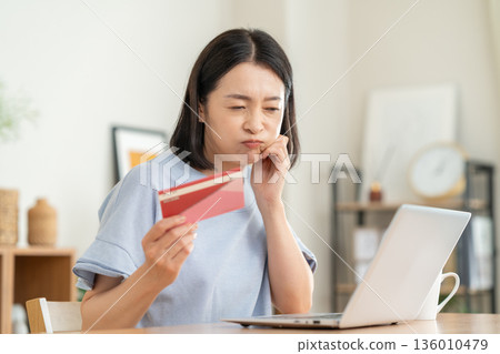 A middle-aged woman looking at her savings passbook in the living room 136010479
