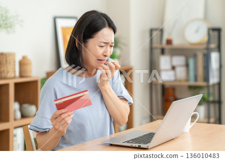 A middle-aged woman looking at her savings passbook in the living room A middle-aged woman looking at her savings passbook in the living room 136010483