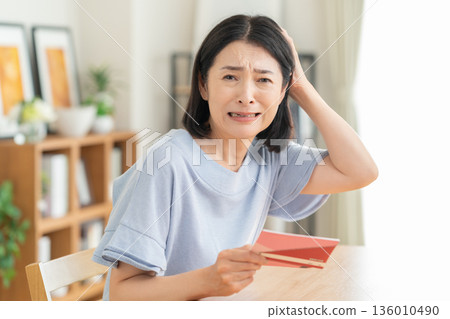 A middle-aged woman looking at her savings passbook in the living room 136010490