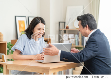 A businessman discussing business with a woman in the living room A businessman discussing business with a woman in the living room 136010509