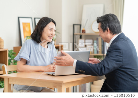 A businessman discussing business with a woman in the living room A businessman discussing business with a woman in the living room 136010510