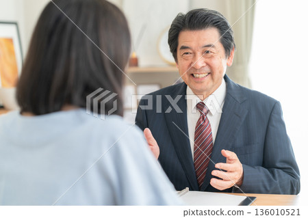 A businessman discussing business with a woman in the living room A businessman discussing business with a woman in the living room 136010521