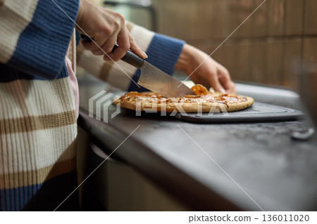 Person slicing pepperoni pizza on kitchen counter Person slicing pepperoni pizza on kitchen counter 136011020