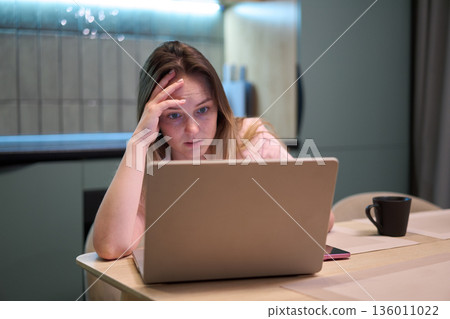 Female concentrating on laptop at kitchen table indoors 136011022