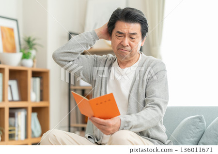 一位中年男子在客廳看著他的退休金簿。 136011671