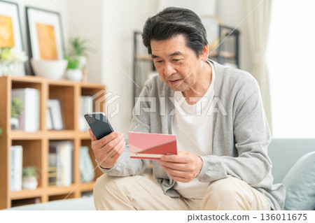 一位中年男子在客廳查看他的儲蓄存摺。 136011675
