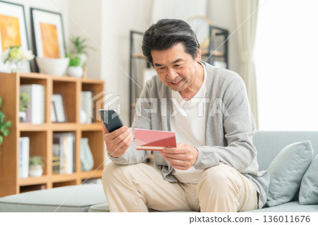 A middle-aged man looking at his savings passbook in the living room A middle-aged man looking at his savings passbook in the living room 136011676