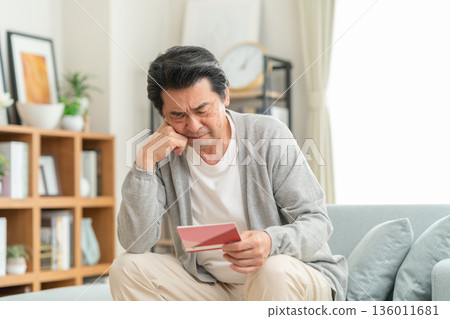 A middle-aged man looking at his savings passbook in the living room A middle-aged man looking at his savings passbook in the living room 136011681