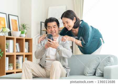 A middle-aged couple watching a smartphone in the living room A middle-aged couple watching a smartphone in the living room 136011686