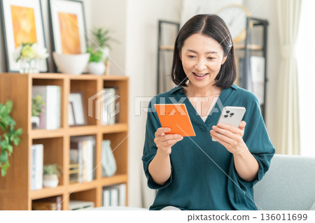 A middle-aged woman looking at her pension book in the living room A middle-aged woman looking at her pension book in the living room 136011699