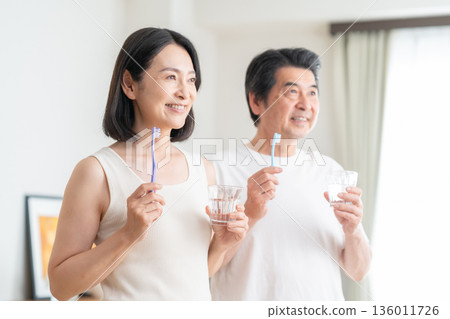 A middle-aged couple brushing their teeth in the living room 136011726