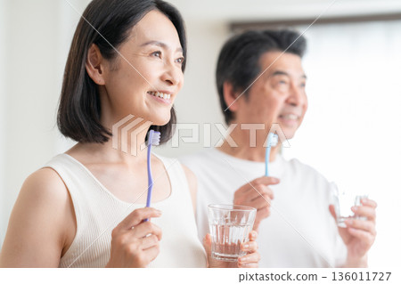A middle-aged couple brushing their teeth in the living room 136011727