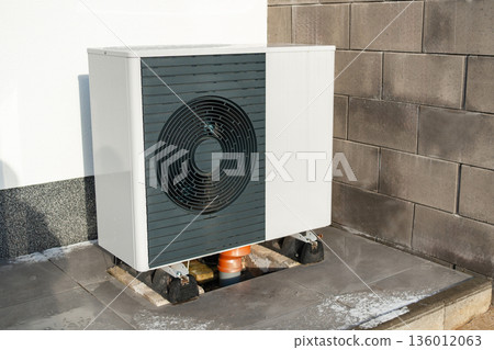 Outdoor heat pump or air conditioning unit installed on residential building. Modern energy efficient heating technology 136012063