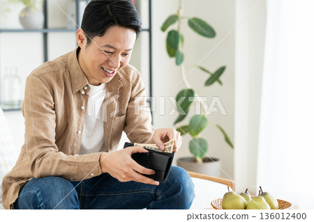 Middle-aged man holding a wallet in the living room 136012400