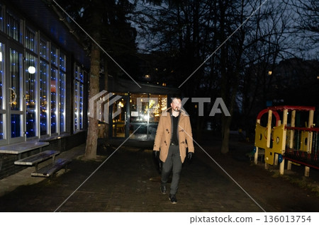 Evening stroll through the park amid vibrant lights and shadows, a man enjoys a tranquil walk as night descends and the city comes alive with decor Evening stroll through the park amid vibrant lights and shadows, a man enjoys a tranquil walk as night descends and the city comes alive with decor 136013754