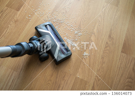 Vacuum cleaner nozzle sucking up spilled rice grains from an oak parquet floor, showing home cleaning and house chores 136014073