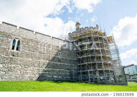 Historic stone Windsor Castle with scaffolding erected for construction under a bright blue sky and floating clouds. A streetscape on the outskirts of London 136015699